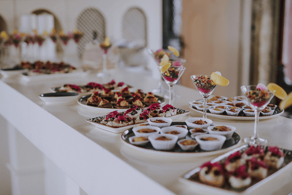 Szwedzki stół z różnorodnym cateringiem: estetyczne przekąski finger foods na półmiskach, muffiny oraz kolorowe sałatki w kieliszkach martini.